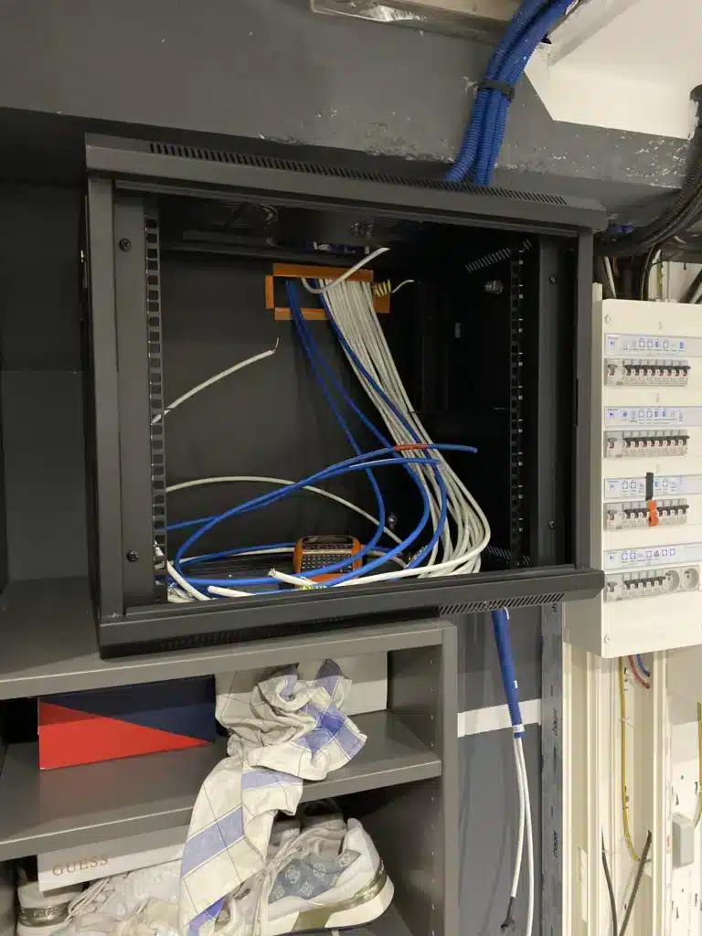 Baie de brassage informatique fixée au mur d'une buanderie avec arrivée des câbles réseau par l'arrière.